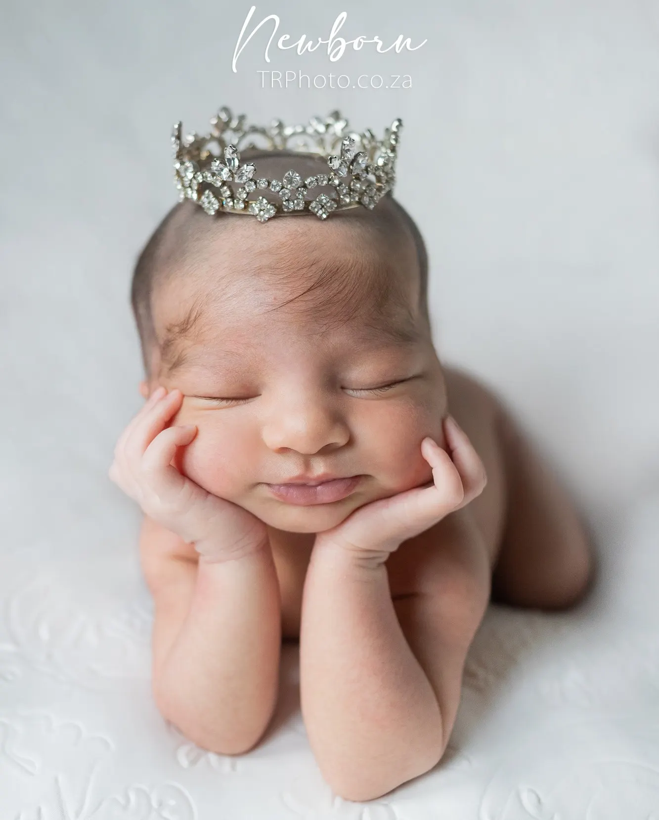 A posed newborn wearing a small crown